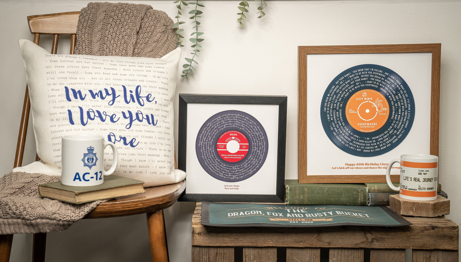 Framed personalised song lyric prints designed like vinyl records displayed on a shelf with books, mugs and a decorative cushi