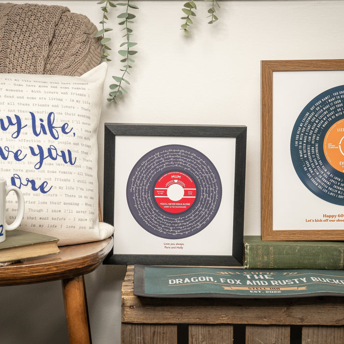 Framed personalised song lyric prints designed like vinyl records displayed on a shelf with books, mugs and a decorative cushi