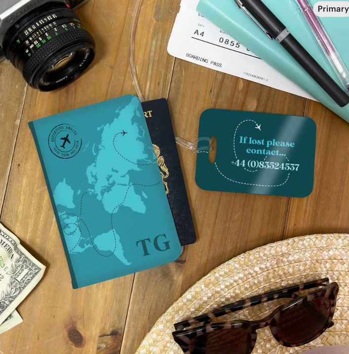 A teal personalised passport holder and matching luggage tag set displayed on a wooden table. The passport cover features a minimalist world map design with flight path lines, the initials “TG,” and the phrase “Adventure Awaits.” The luggage tag reads “If lost please contact…” followed by a phone number. Items like a passport, sunglasses, and a camera create a travel-themed flat lay.