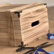 Wooden box with decorative brackets on a table with scissors and blue tape.