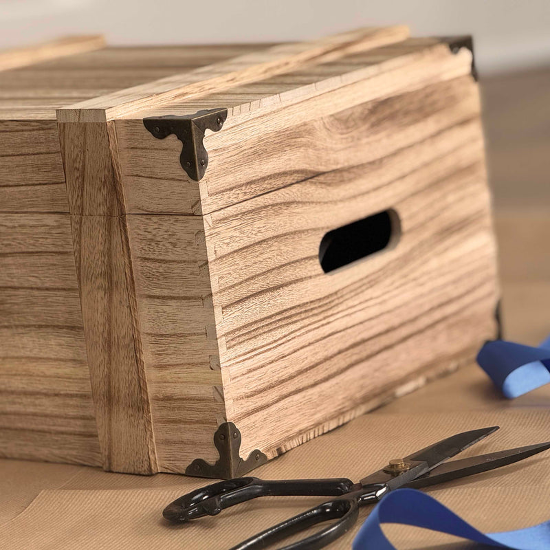 Wooden box with decorative brackets on a table with scissors and blue tape.