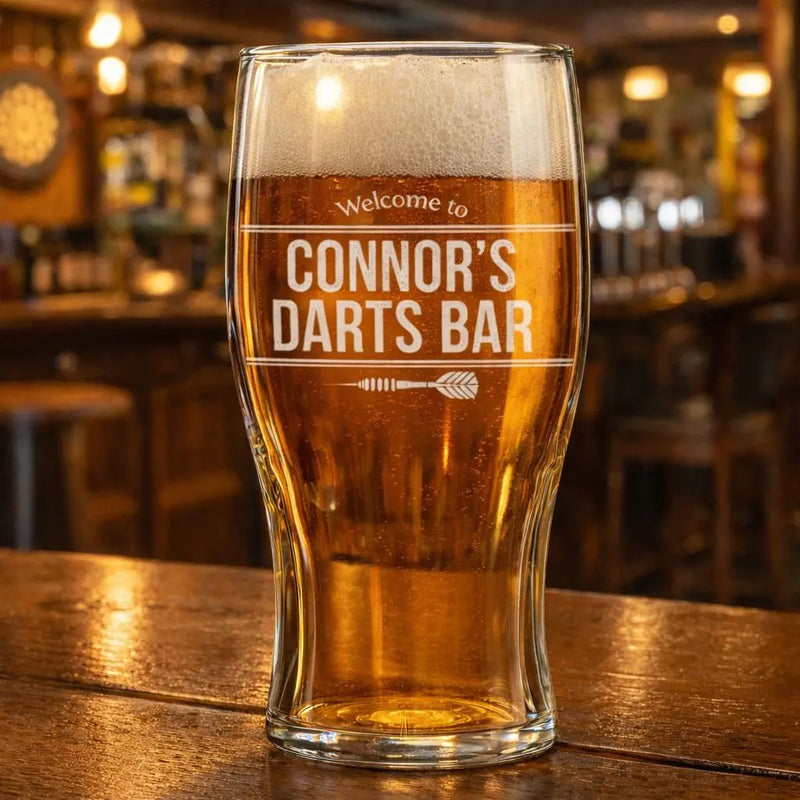 Engraved personalised darts bar pint glass filled with beer, displayed on a pub bar counter.