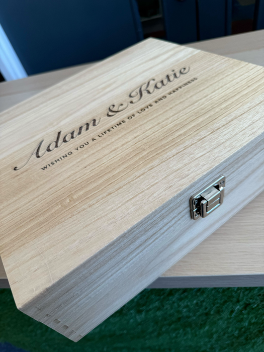 Engraved wooden wine box featuring names “Adam & Katie” and a love message, shown on a wooden tabletop with metal clasp visible.