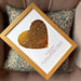 Framed gold foil heart print reading “How much a heart can hold,” personalised with couple’s names and anniversary date, resting on a patterned cushion.