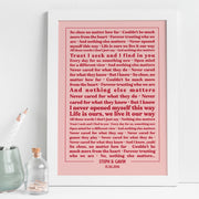 A framed lyric print with a white frame and dusty rose background, displayed on a white desk with a small vase, pencil pot, and decorative bottle. The text showcases lyrics from “Nothing Else Matters” in red type, with emphasis on lines such as “Trust I seek and I find in you” and “Life is ours, we live it our way.” The personalization at the bottom reads “STEPH & GAVIN – 15.06.2016,” giving the artwork a romantic, modern look.