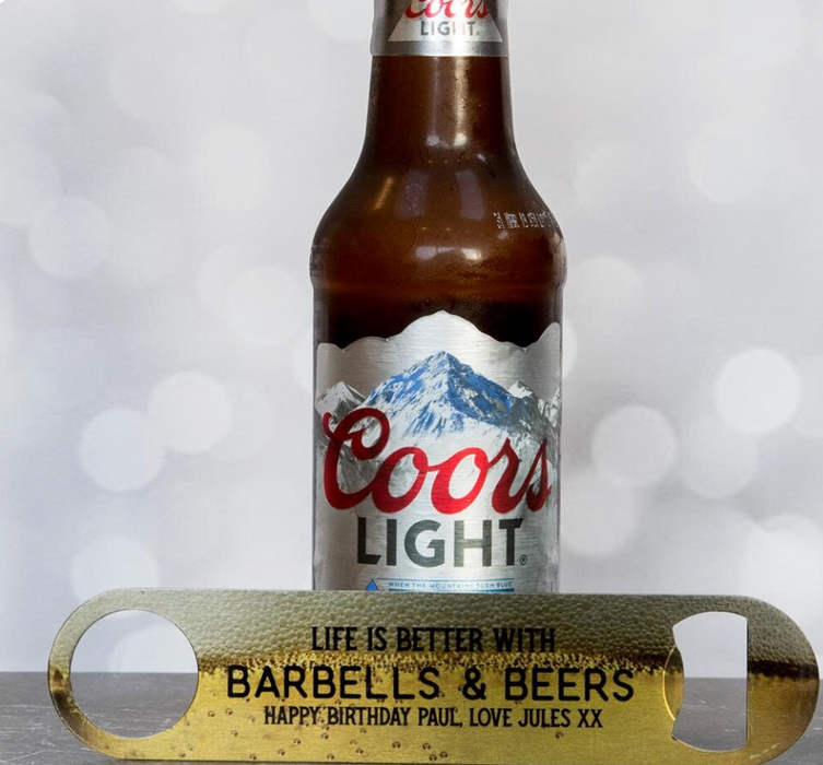 Personalised gold bottle opener engraved with “Life Is Better With Barbells & Beers” and birthday message, displayed in front of a Coors Light beer bottle.