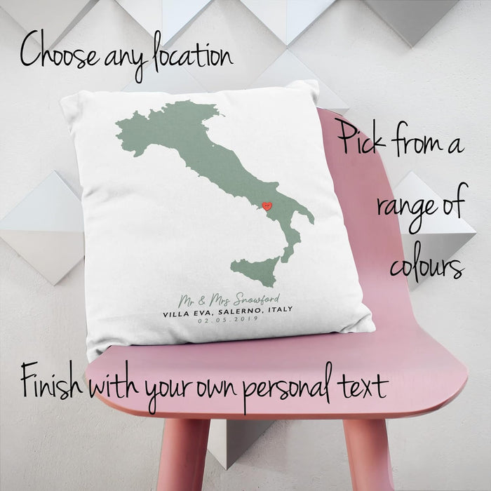 Personalised map cushion with green silhouette of Italy and red heart marking a location, customised with names, venue and date, styled on a pink chair with overlay text promoting personalisation options.
