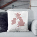 Personalised wedding cushion with blush pink map of the UK and red heart location marker, printed with names and venue details, placed on a grey sofa with black cushion.