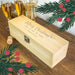 Personalised wooden champagne gift box engraved with “Merry Christmas” message, displayed with festive decorations, champagne glasses, and a cork on a wooden table.