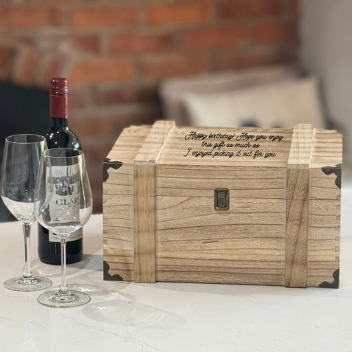 Personalised wooden wine chest engraved with a birthday message, styled with two wine glasses and a bottle of red wine on a marble surface against a brick background.