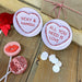 Romantic flat lay with two personalised love heart coasters, heart-shaped lollipops, and wrapped gifts, creating a Valentine’s Day gift aesthetic.