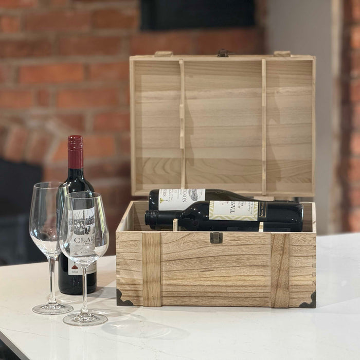 Rustic wooden wine chest open to reveal compartments holding wine bottles, displayed with glasses and a red wine bottle beside it.
