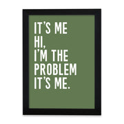 A framed minimalist quote print with a sage green background and bold white text that reads: “It’s me, hi, I’m the problem, it’s me.” The design is housed in a sleek black frame with a modern, graphic feel.