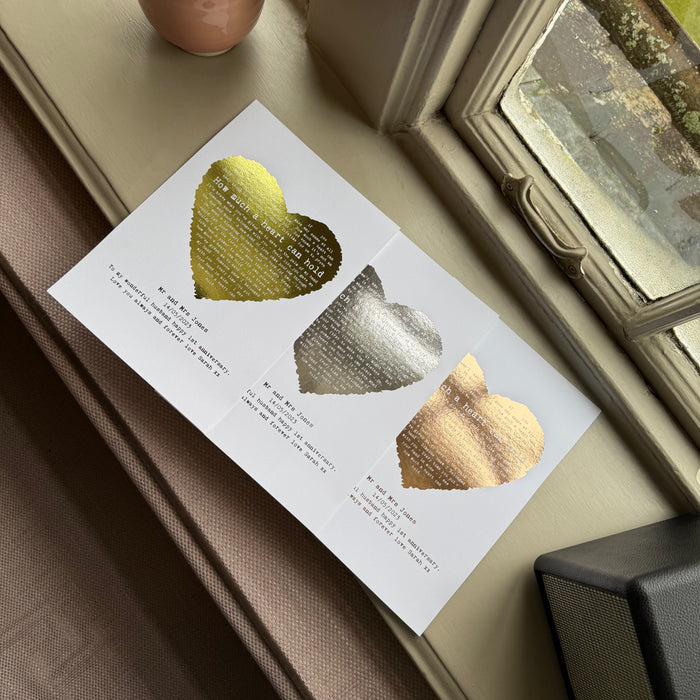 Set of three personalised heart lyric prints in gold, silver and rose gold foil finishes, featuring song lyrics and names, displayed on a windowsill.