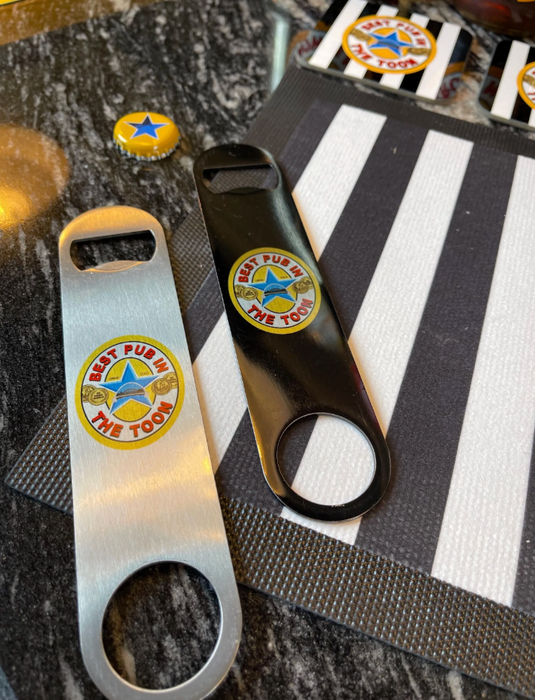 Silver and black “Best Pub in The Toon” bar blade openers displayed on a black-and-white striped surface beside bottle caps — perfect gift for football fans and home bars.