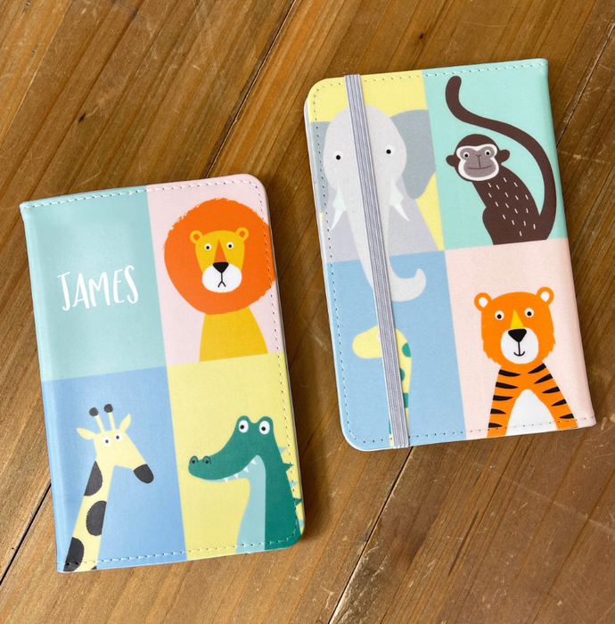 Two animal-themed children’s passport holders with colourful safari illustrations. One shows the name “James” on the front, while the other displays the reverse side with an elastic strap and more animal characters including a monkey, elephant, and tiger.