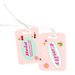 Two matching pink luggage tags with fun sticker-style graphics including cherries, hearts, flowers, sunglasses, and smiley faces. Each tag is personalised — one with the name Emily and the other with Reid, city, and contact details — attached to clear plastic loops for securing to luggage.