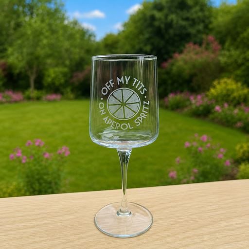 Engraved Off My Tits on Aperol Spritz wine glass in a garden setting