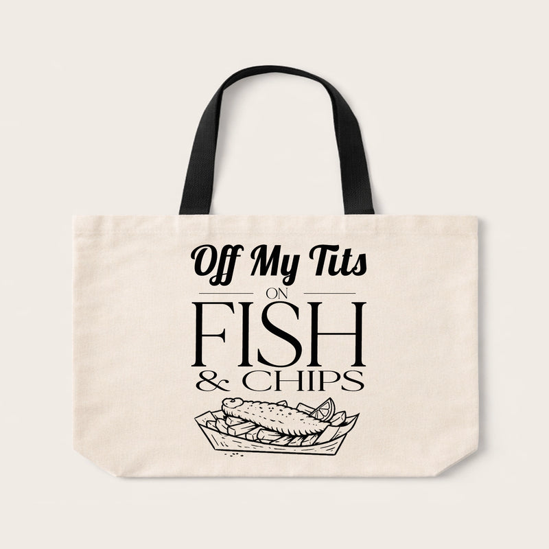 An off-white canvas tote bag with black handles and a black graphic print that reads 'Off My Tits ON FISH & CHIPS' above a fish in a tray illustration, shown on a light beige background.