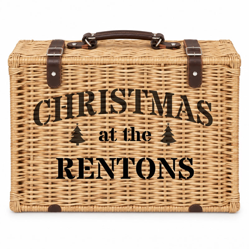 A rectangular woven wicker picnic basket with a dark brown handle and straps, featuring the black printed text 'CHRISTMAS at the RENTONS' on the front, set against a plain white background.