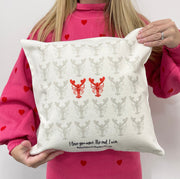 Person holding a white cushion with grey and red lobster pattern and the phrase “I love you more. The end. I win.” printed at the bottom.