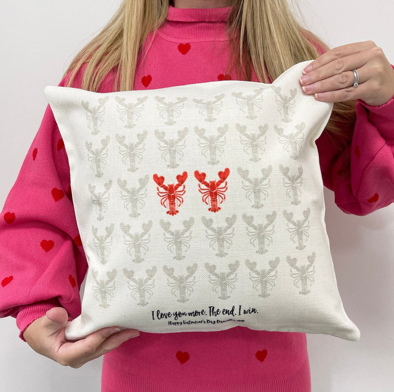 Person holding a white cushion with grey and red lobster pattern and the phrase “I love you more. The end. I win.” printed at the bottom.