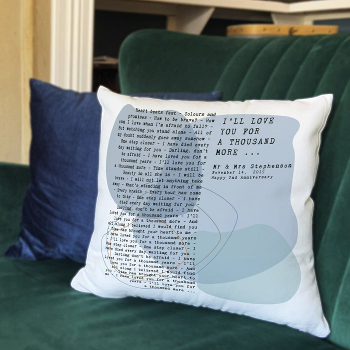 Personalised lyric cushion printed with the words “I’ll love you for a thousand more” and song text from “A Thousand Years,” featuring names and anniversary details, displayed on a green velvet sofa.