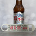 Personalised metal bottle opener engraved with “The Greatest Husband on Earth” and anniversary details, displayed in front of a Coors Light beer bottle on a grey surface.